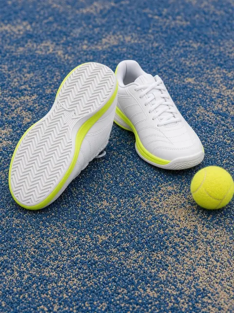 White and neon yellow court shoes showing a herringbone sole on blue padel turf with a ball